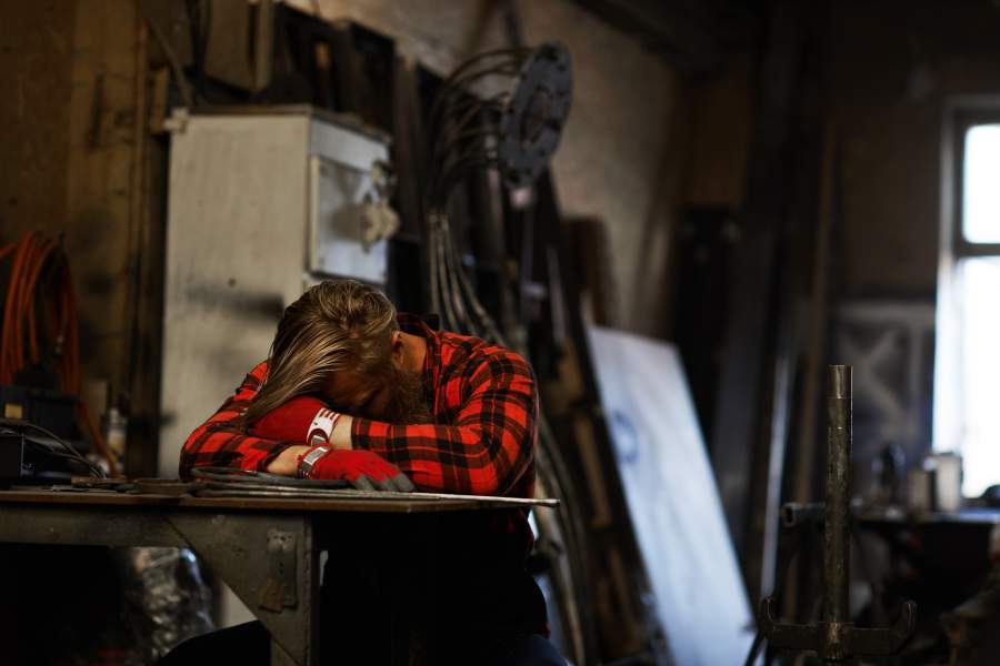 El trabajador cansado y fatigado que duerme con la cabeza sobre los brazos en una mesa en el ambiente de trabajo necesita descansar un poco para reducir la fatiga.