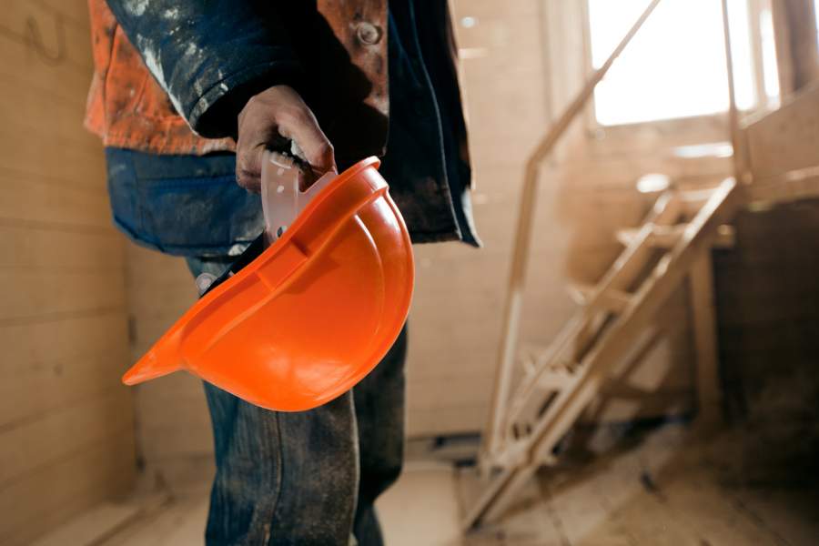 El trabajador tiene un nuevo casco naranja en la mano en el sitio de construcción